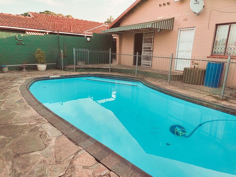 Outdoor pool area featuring a swimming pool, stone paving, and metal security fencing adjacent to the rear building elevation.