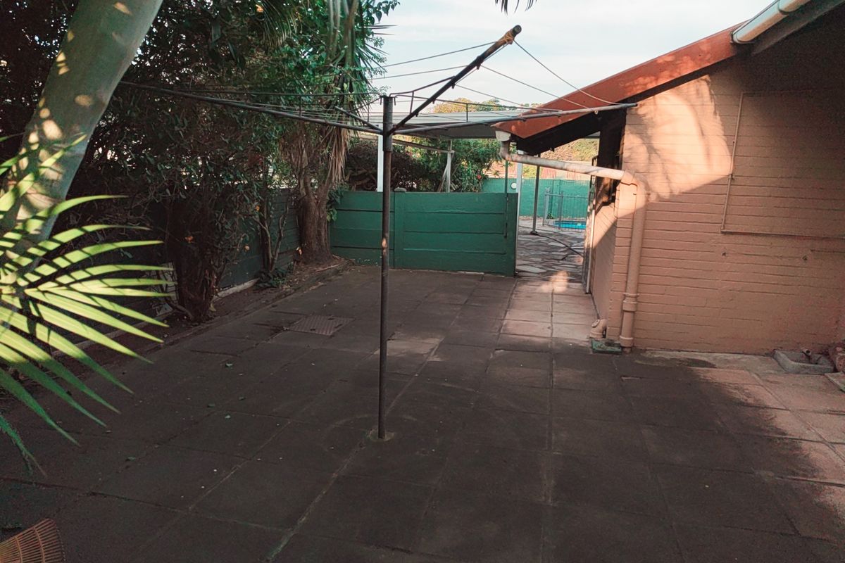 Rear exterior area featuring a paved patio, brick walling, and a rotary clothesline, providing access to the garden and pool area.