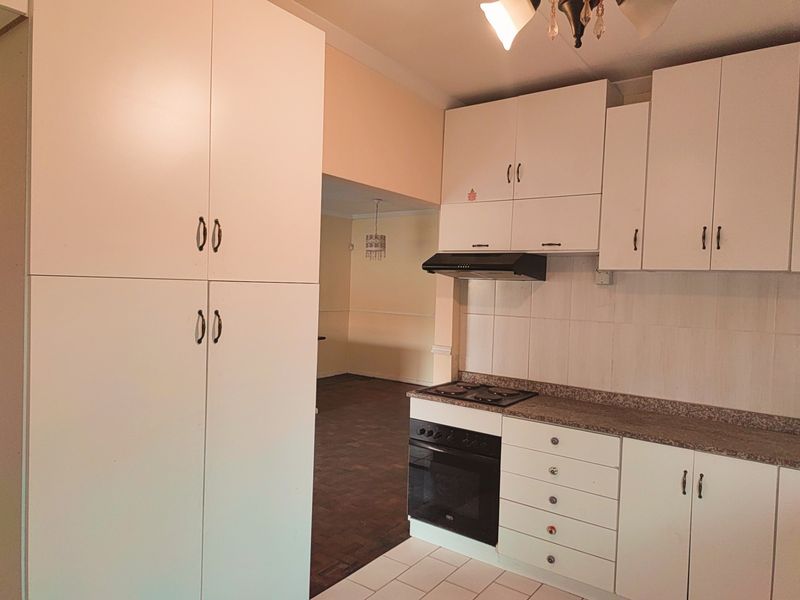 A functional kitchen featuring white built-in cabinetry, laminate countertops, a built-in oven with hob, and an extractor fan, with tiled flooring and backsplash.