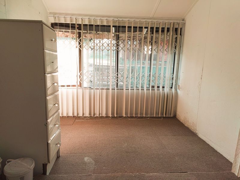 A bedroom featuring carpet flooring, vertical blinds, and a security gate on the window, showing signs of wear and requiring cosmetic updates.