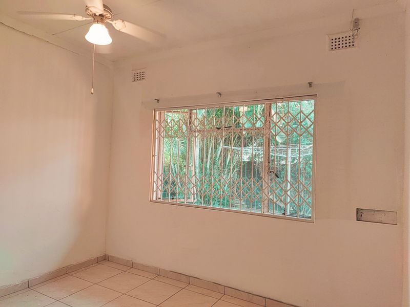A vacant bedroom featuring tiled flooring, a ceiling fan, and a window fitted with a security gate.