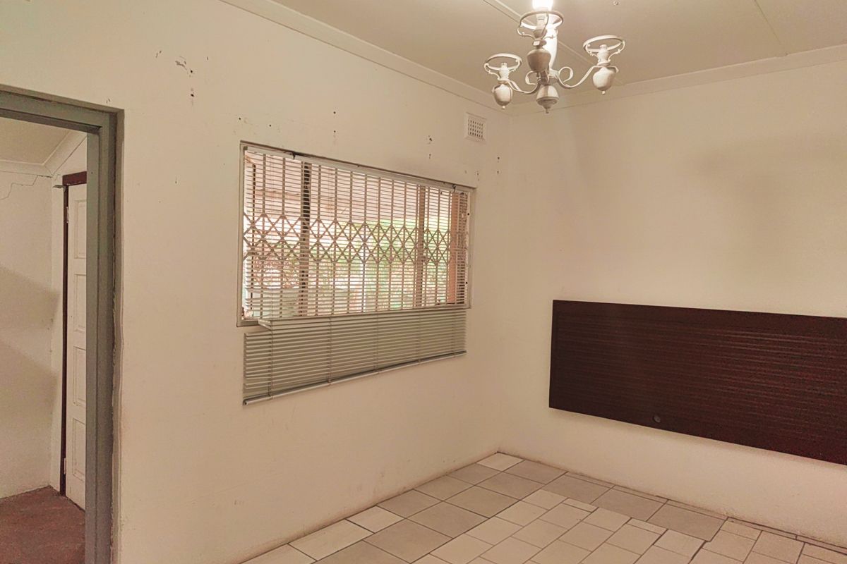 An empty bedroom featuring tiled flooring, a security gate on the window, and a wall-mounted headboard, requiring cosmetic updates to improve its condition.