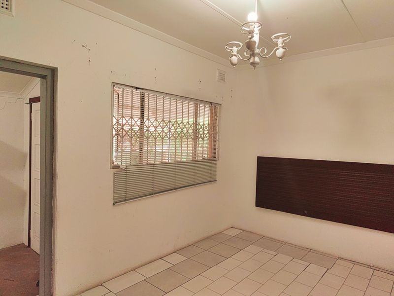 An empty bedroom featuring tiled flooring, a security gate on the window, and a wall-mounted headboard, requiring cosmetic updates to improve its condition.