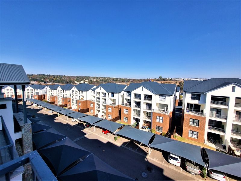 An elevated aerial view of an apartment complex featuring multiple residential blocks with pitched roofs, brick detailing, and covered parking bays.