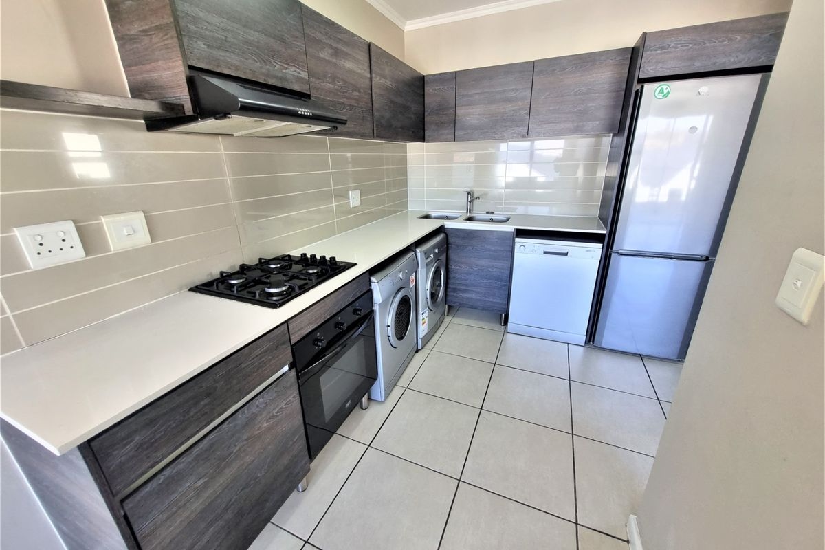 Modern kitchen featuring dark wood-grain cabinetry, white countertops, gas hob, extractor fan, built-in oven, and tiled flooring with integrated appliance spaces.