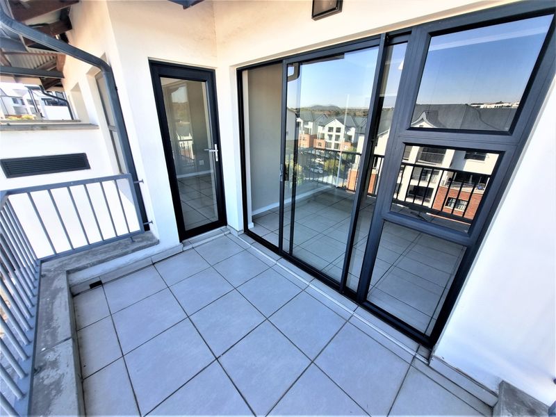 A clean, modern balcony featuring tiled flooring, a metal balustrade, and large sliding glass doors providing access to the apartment interior.