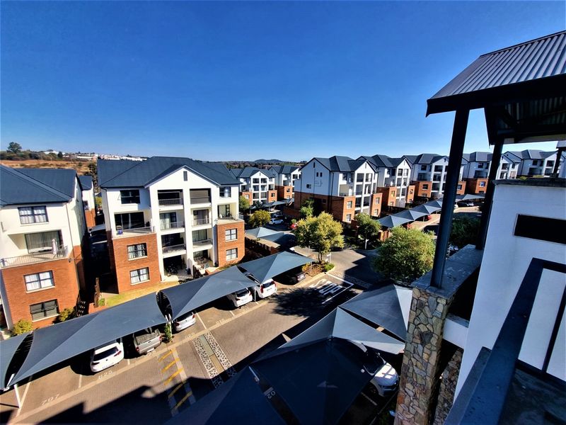 Aerial view of a modern apartment complex featuring brick and plaster facades, metal roofing, and covered parking bays with shade sails.