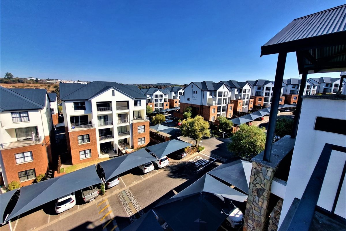 Aerial view of a modern apartment complex featuring brick and plaster facades, metal roofing, and covered parking bays with shade sails.