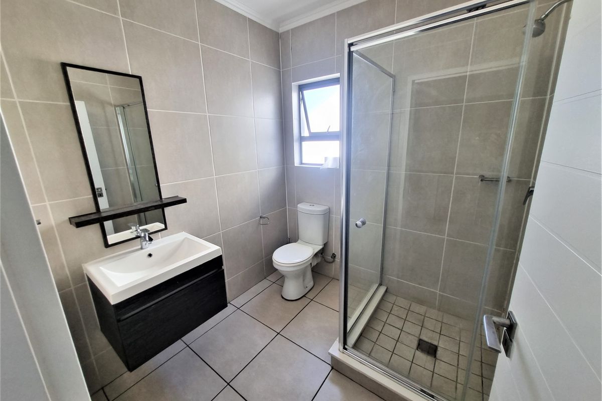 A modern, well-maintained bathroom featuring neutral floor-to-ceiling tiling, a sleek vanity with basin, a toilet, and a glass-enclosed shower.