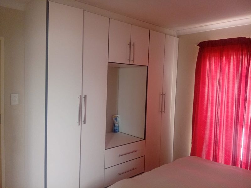 A bedroom featuring a modern white built-in wardrobe with integrated drawers and shelving, providing ample storage space.