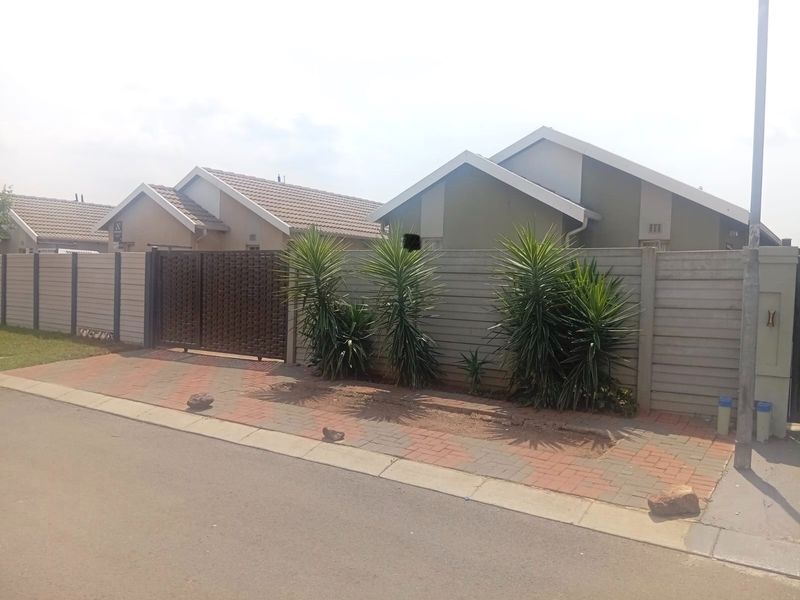 Street view of a residential property featuring a precast concrete boundary wall, metal driveway gate, and paved verge area.