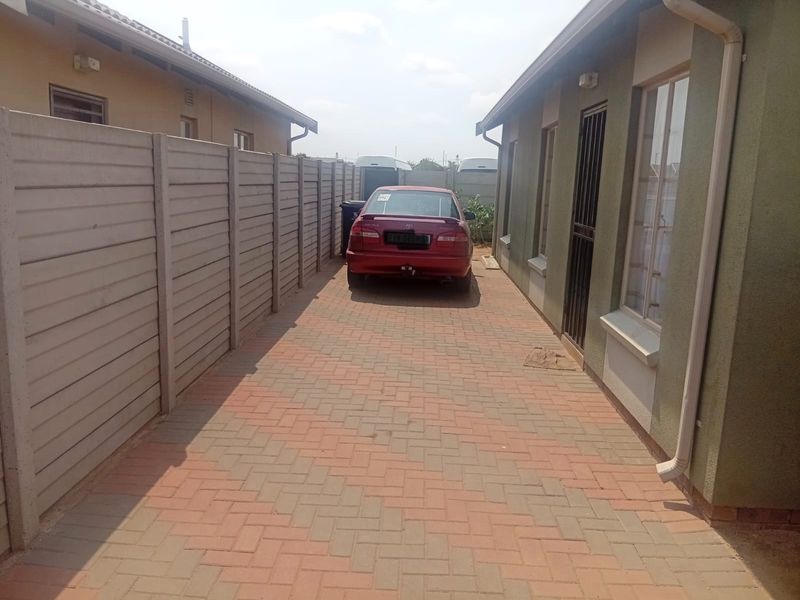A side exterior view of the property featuring a paved driveway, precast concrete boundary wall, and external building finishes.
