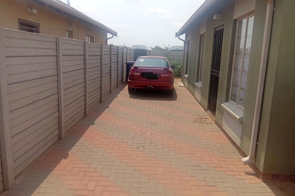 A side exterior view of the property featuring a paved driveway, precast concrete boundary wall, and external building finishes.