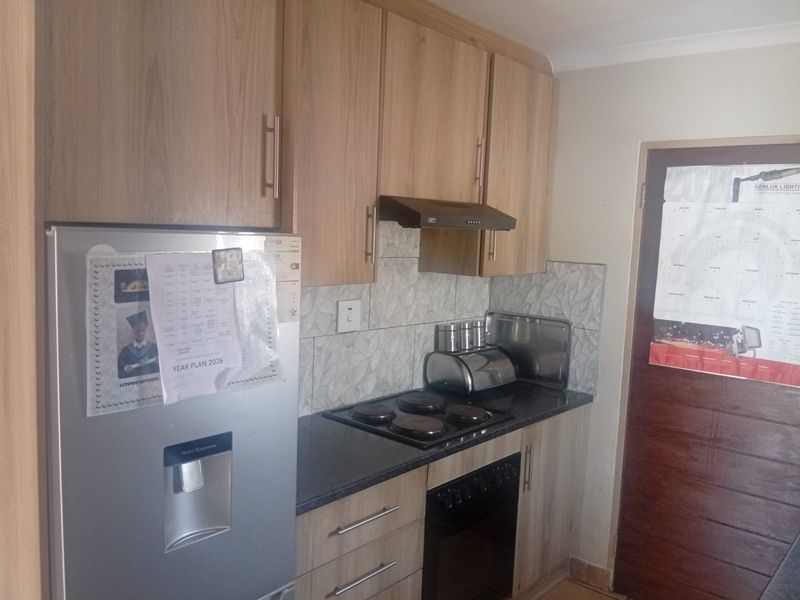 Compact kitchen featuring light wood-finish cabinetry, dark countertops, a built-in oven with hob, and a tiled backsplash.