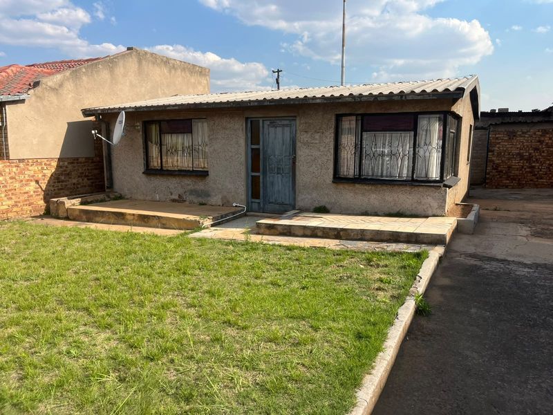Front view of a single-story house featuring a tiled porch, security gates, and a small front garden with a concrete driveway.