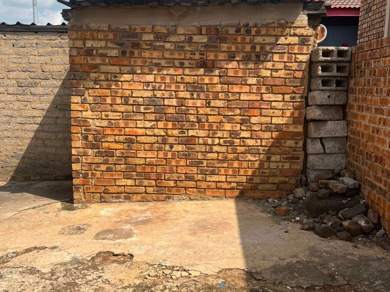 A rear exterior area featuring exposed brick walls, corrugated roofing, and weathered concrete paving with visible surface damage.