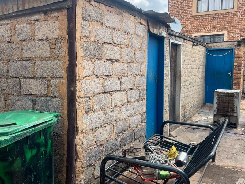 Rear exterior area featuring concrete block outbuildings with paved flooring, showing significant signs of wear and requiring maintenance.