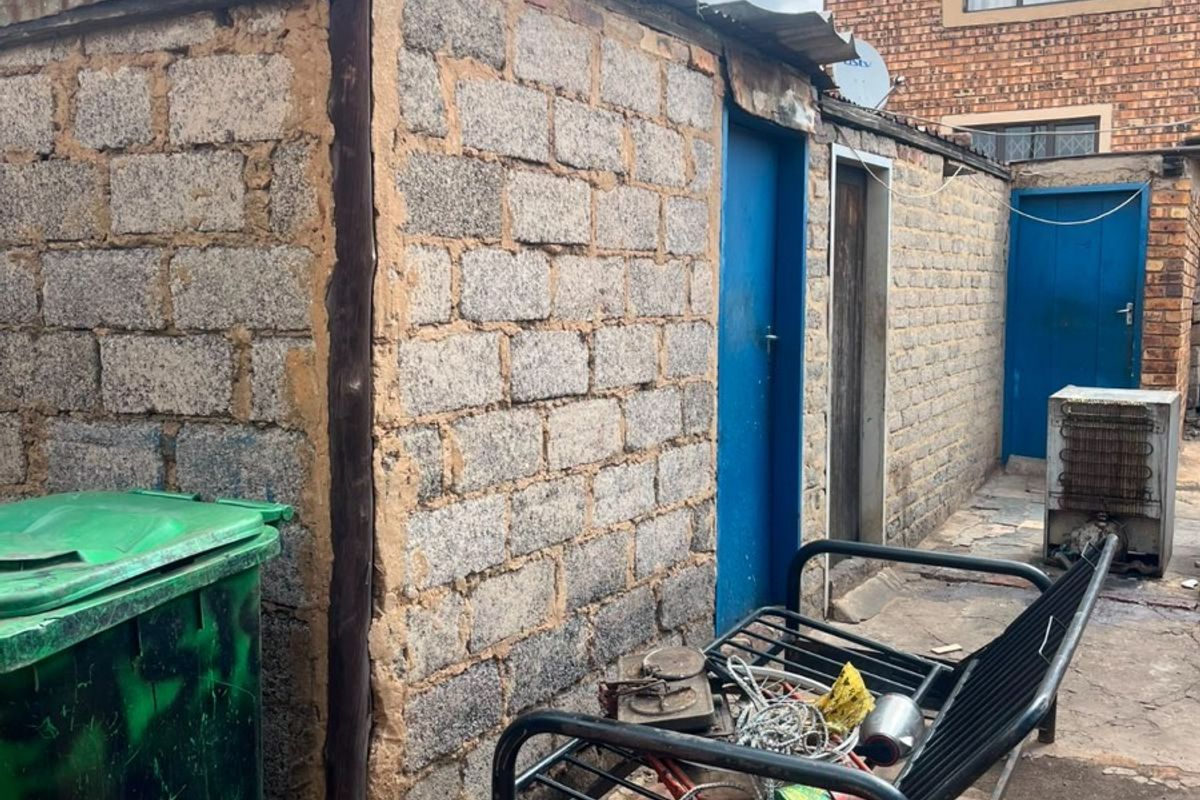 Rear exterior area featuring concrete block outbuildings with paved flooring, showing significant signs of wear and requiring maintenance.