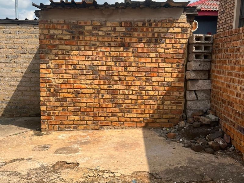Rear exterior area featuring a brick structure with corrugated roofing and weathered concrete paving requiring maintenance.