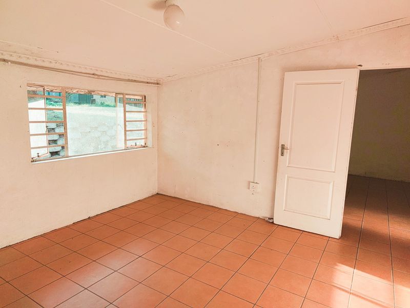 An empty bedroom featuring tiled flooring, a metal-framed window, and a standard internal door, presenting a blank canvas for renovation or interior design.