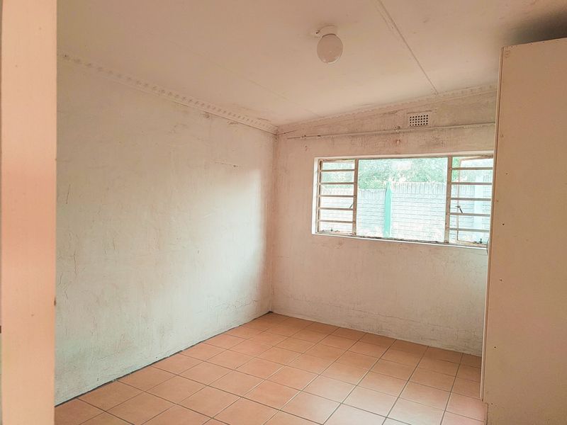 An empty bedroom featuring tiled flooring, steel window frames with security bars, and decorative ceiling cornices, requiring cosmetic updates to the wall finishes.