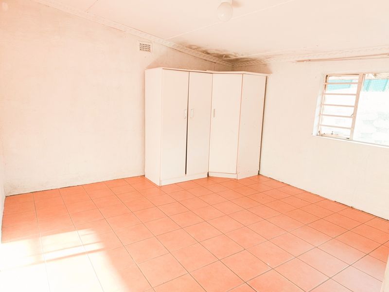 An empty bedroom featuring tiled flooring, security bars on the window, and visible ceiling damage requiring maintenance.