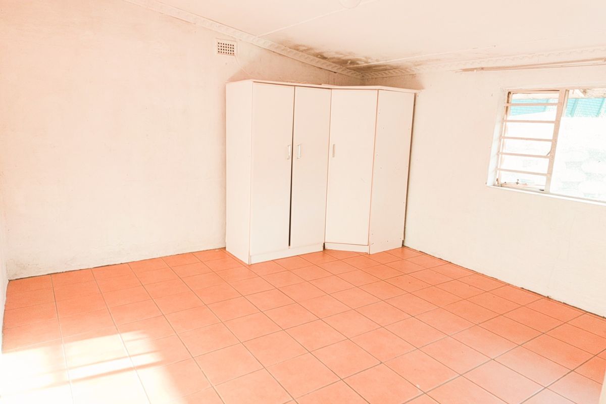 An empty bedroom featuring tiled flooring, security bars on the window, and visible ceiling damage requiring maintenance.
