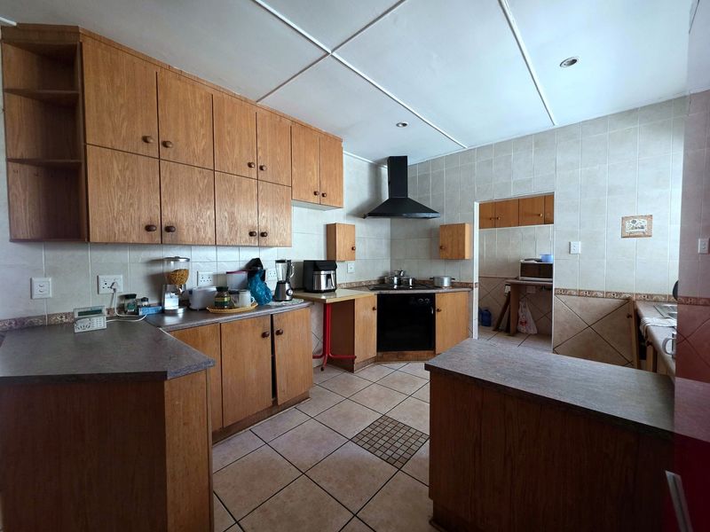 A functional kitchen featuring wooden cabinetry, laminate countertops, a built-in oven with extractor fan, and tiled flooring, offering a classic layout with a separate scullery area.