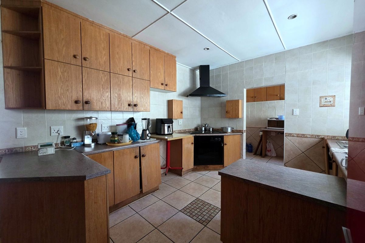 A functional kitchen featuring wooden cabinetry, laminate countertops, a built-in oven with extractor fan, and tiled flooring, offering a classic layout with a separate scullery area.