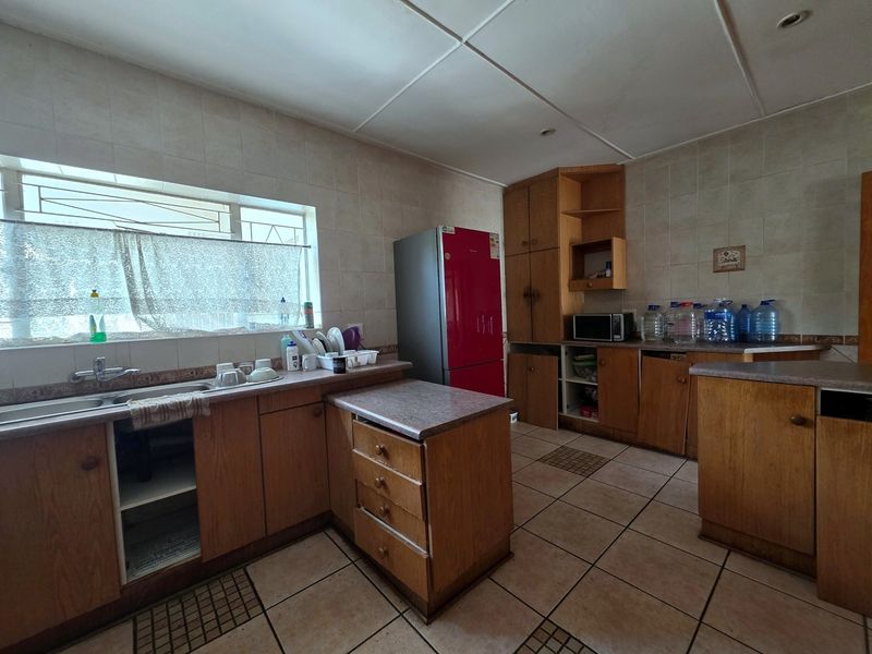 A dated kitchen featuring laminate cabinetry, tiled splashbacks, and ceramic flooring, offering significant potential for modernization and renovation.
