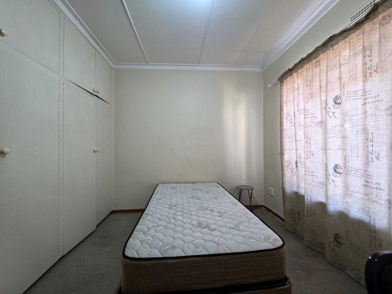 A simple bedroom featuring built-in cupboards, carpeted flooring, and a window with curtains. The room is vacant and ready for a refresh.