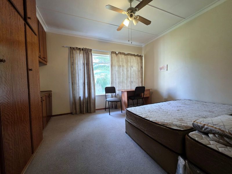 A functional bedroom featuring built-in wooden cupboards, carpeted flooring, and a ceiling fan, offering a neutral space ready for personalization.