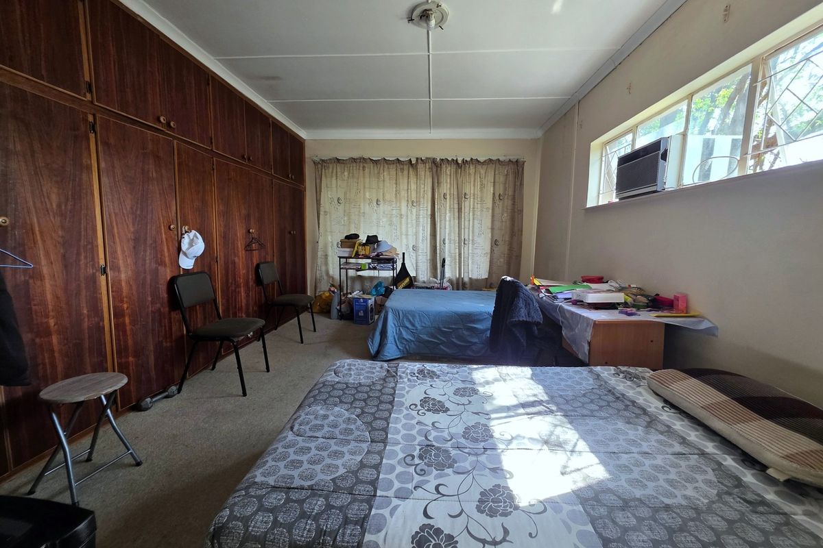 A spacious bedroom featuring extensive built-in wooden cabinetry, carpeted flooring, and a window-mounted air conditioning unit, offering potential for modernization.