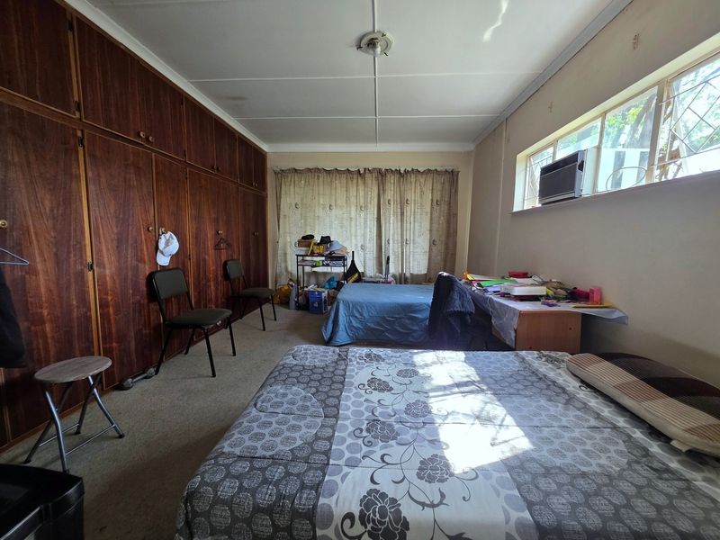 A spacious bedroom featuring extensive built-in wooden cabinetry, carpeted flooring, and a window-mounted air conditioning unit, offering potential for modernization.