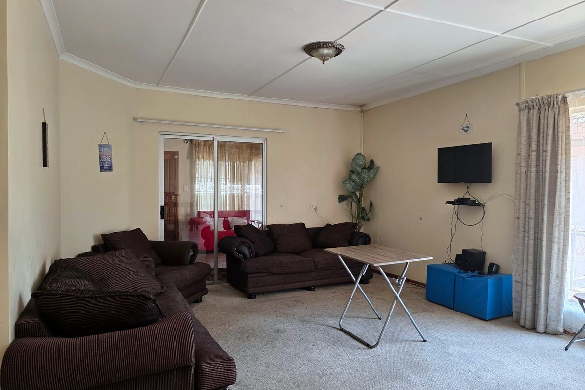 A living room featuring carpet flooring, ceiling tiles, and a sliding glass door providing access to an adjacent space.