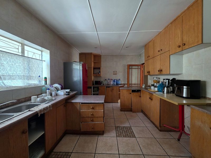 A functional kitchen featuring extensive wooden cabinetry, tiled flooring, and a double bowl sink, offering significant potential for a modern renovation.