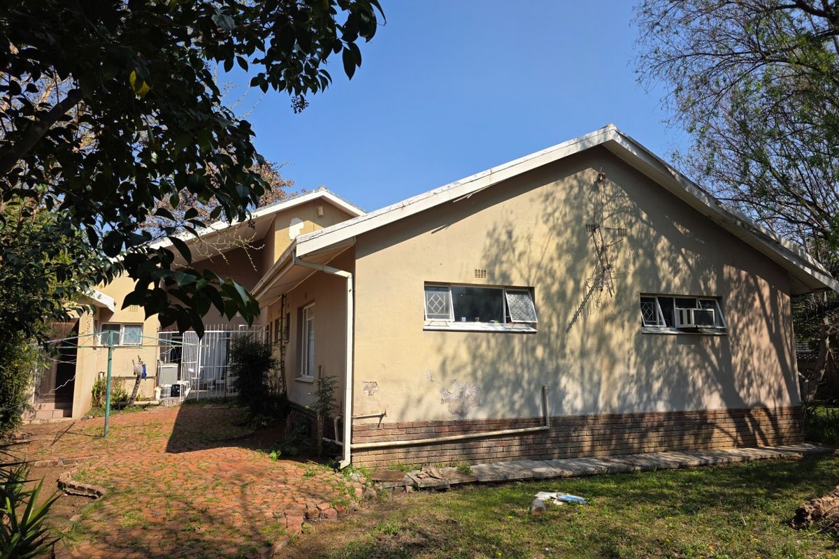 Rear view of the house showing the exterior facade, brick paving, and garden area with visible signs of wear on the plaster and paint.