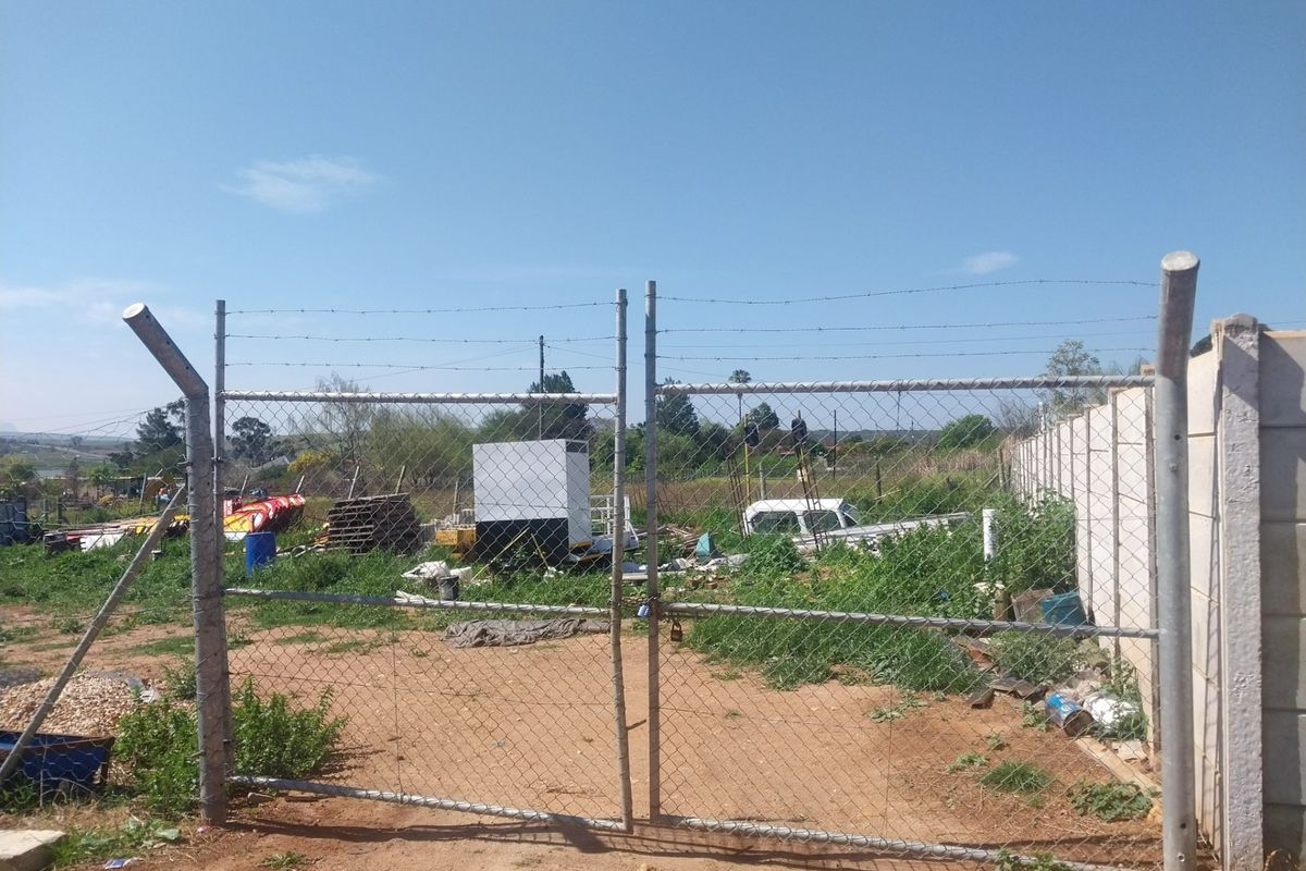 Vacant residential land secured by a chain-link fence, barbed wire, and precast concrete walling, featuring an access gate.