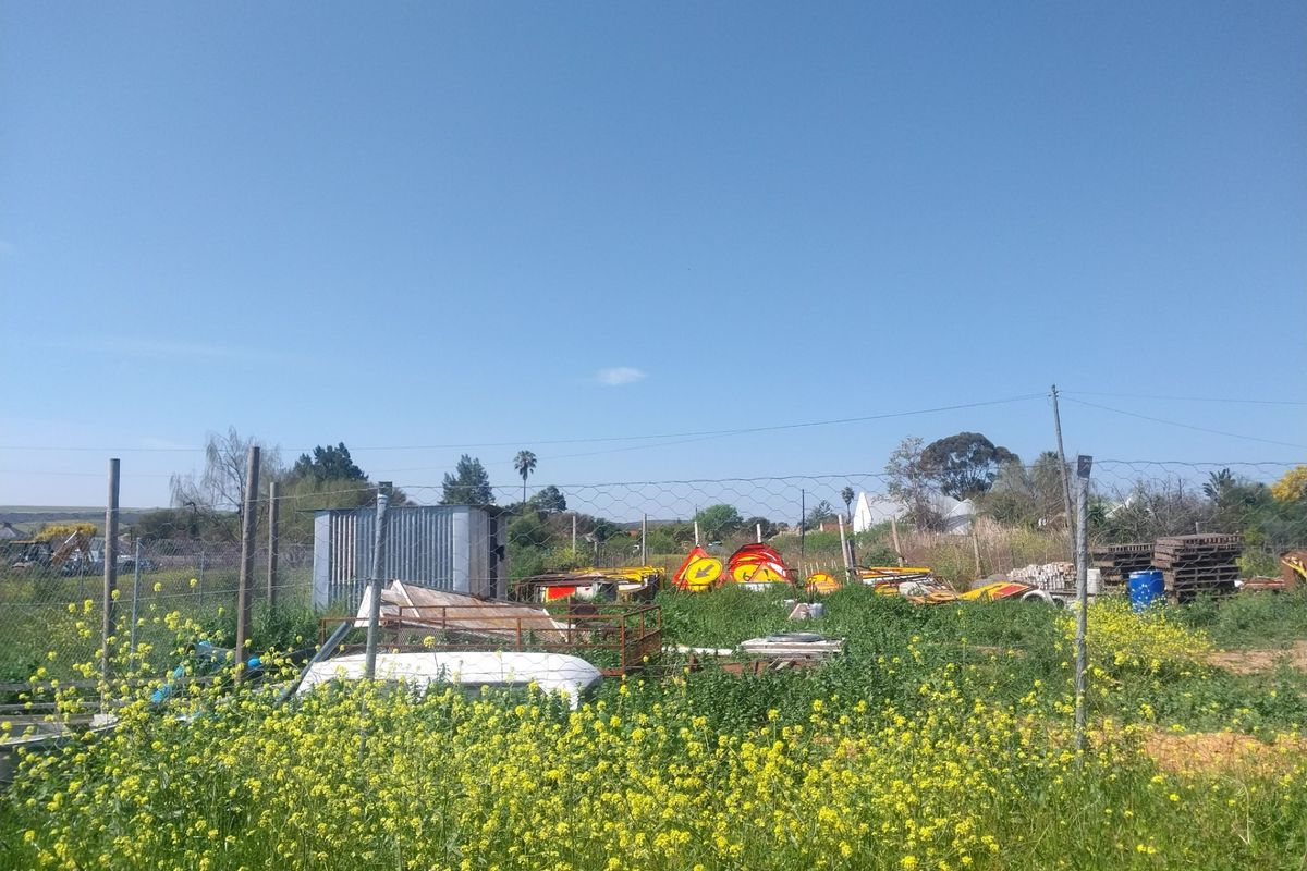 A vacant residential plot featuring overgrown vegetation, wire mesh fencing, and a small metal shed structure on the property.