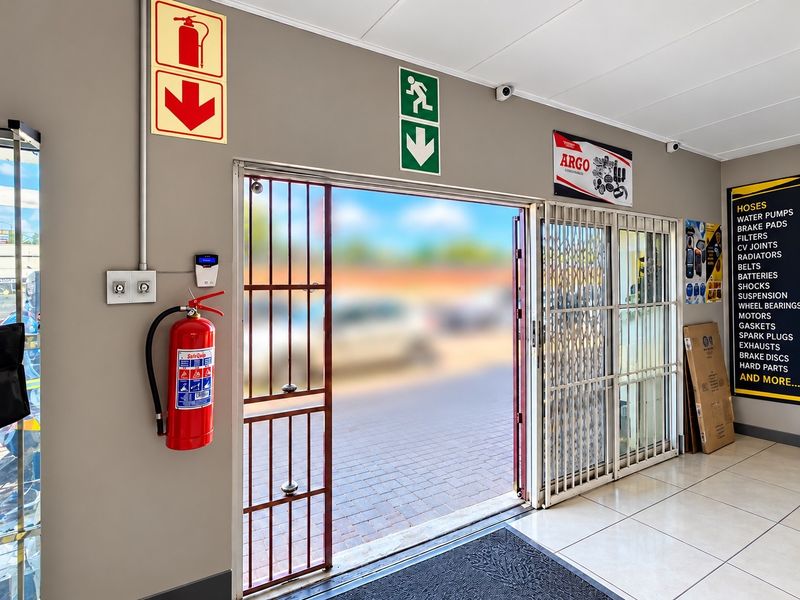 Commercial entrance area featuring tiled flooring, security gate, fire safety equipment, and access control system.