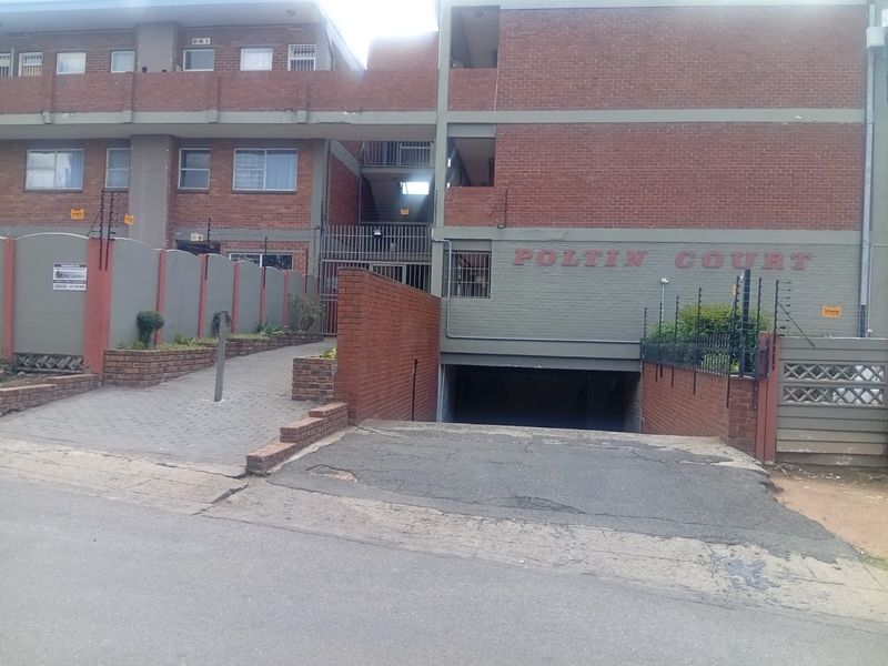 Front exterior view of Poltin Court apartment building featuring a brick facade, secure gated entrance, and underground parking access.