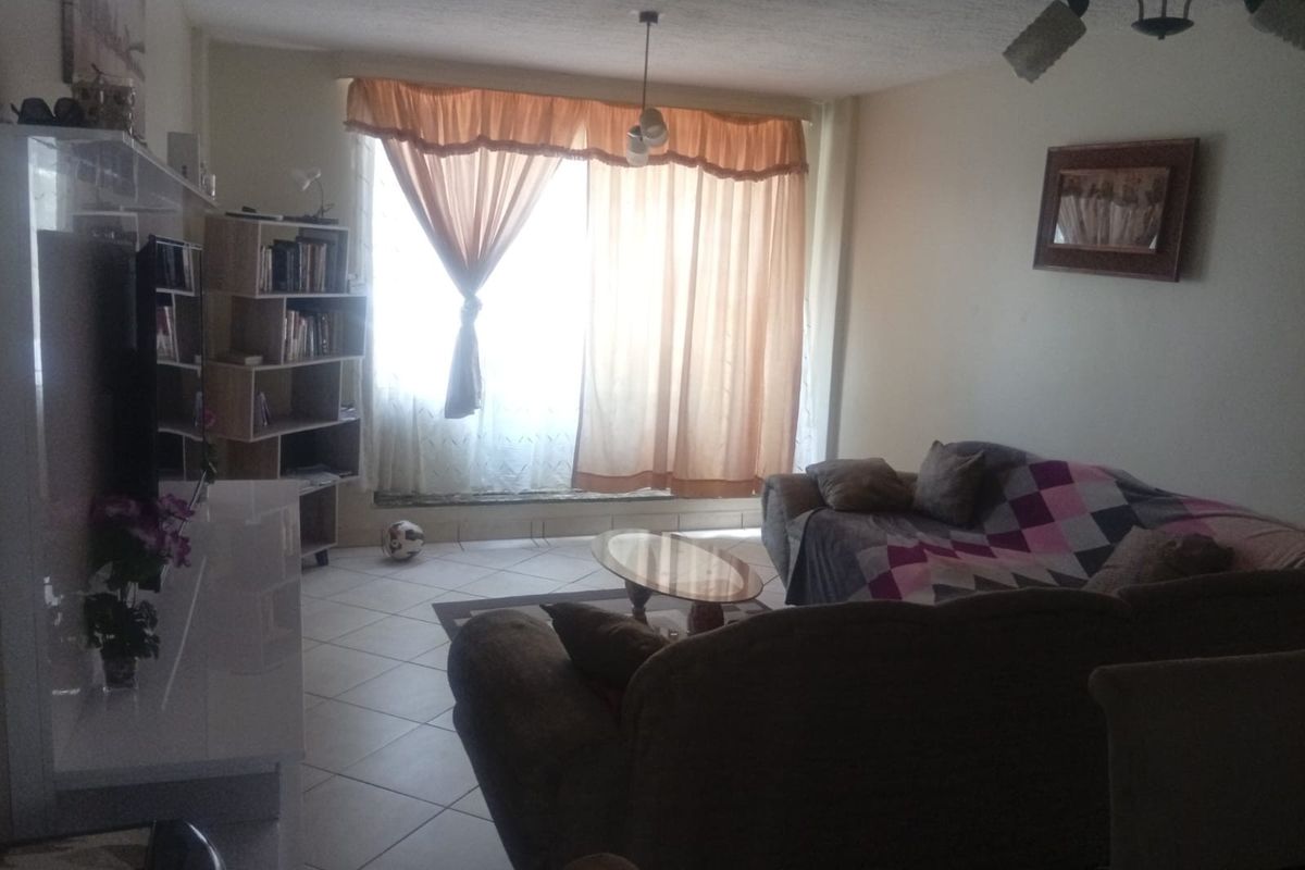 A living room area featuring tiled flooring and natural light from a large window with curtains.