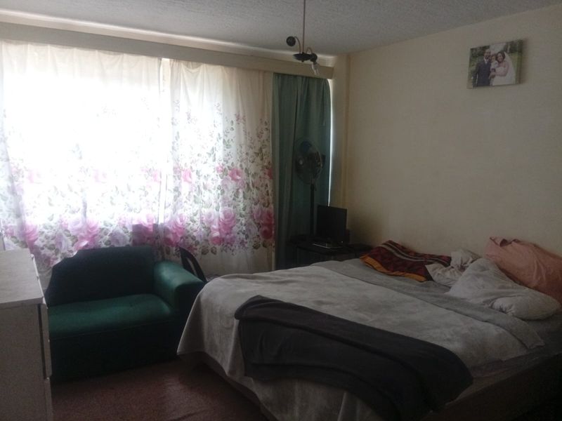A bedroom featuring a large window with curtains and a central ceiling light fixture.