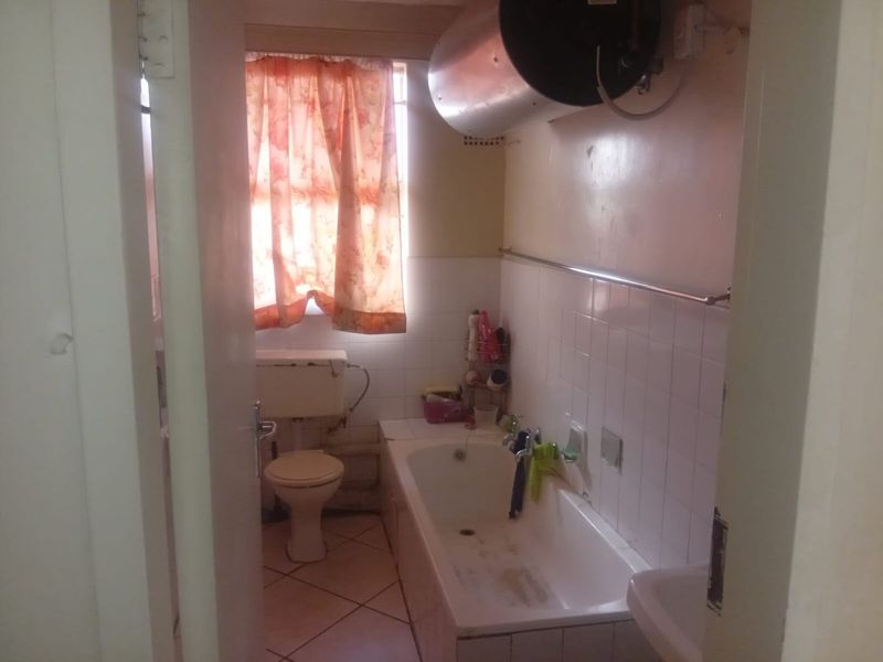 A dated bathroom featuring a bathtub, toilet, and wall-mounted geyser, requiring cosmetic updates and modernization to improve its overall condition and appeal.