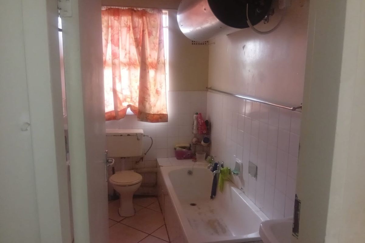 A dated bathroom featuring a bathtub, toilet, and wall-mounted geyser, requiring cosmetic updates and modernization to improve its overall condition and appeal.