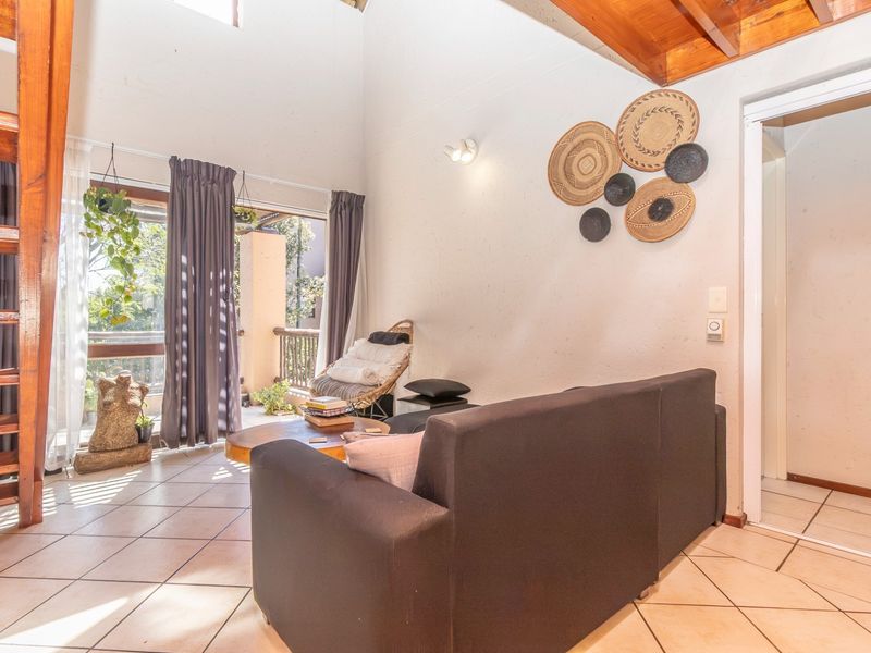 Bright living room featuring high ceilings with exposed timber beams, tiled flooring, and direct access to a private balcony.