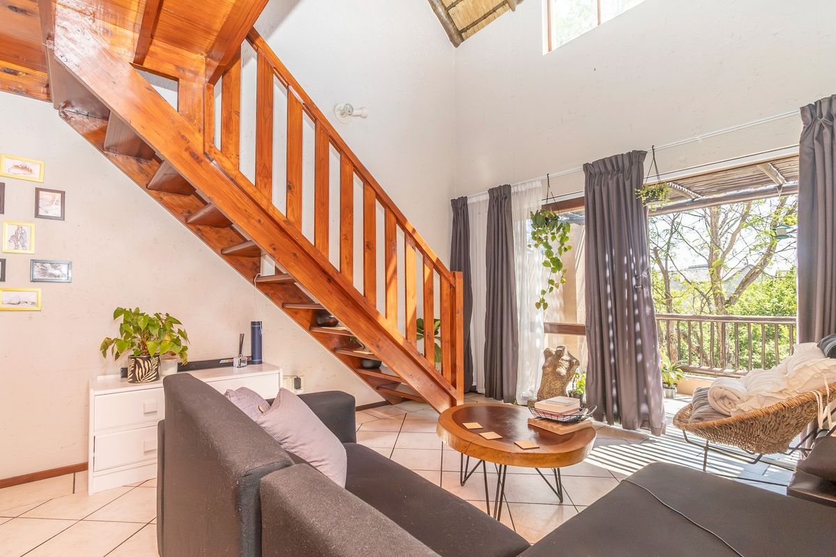 Spacious living room featuring a prominent wooden staircase, vaulted ceilings, and direct access to a private balcony through large sliding glass doors.
