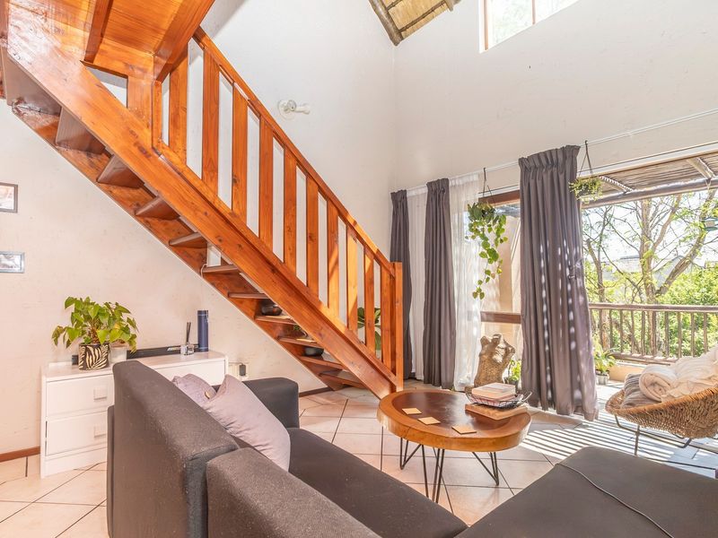 Spacious living room featuring a prominent wooden staircase, vaulted ceilings, and direct access to a private balcony through large sliding glass doors.