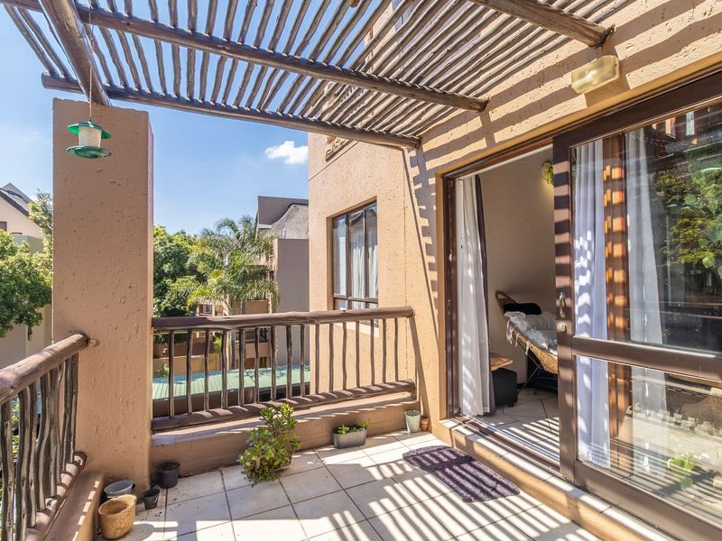 A sunny balcony featuring a wooden pergola, tiled flooring, and a wooden balustrade, providing a pleasant outdoor space accessible via a sliding glass door.
