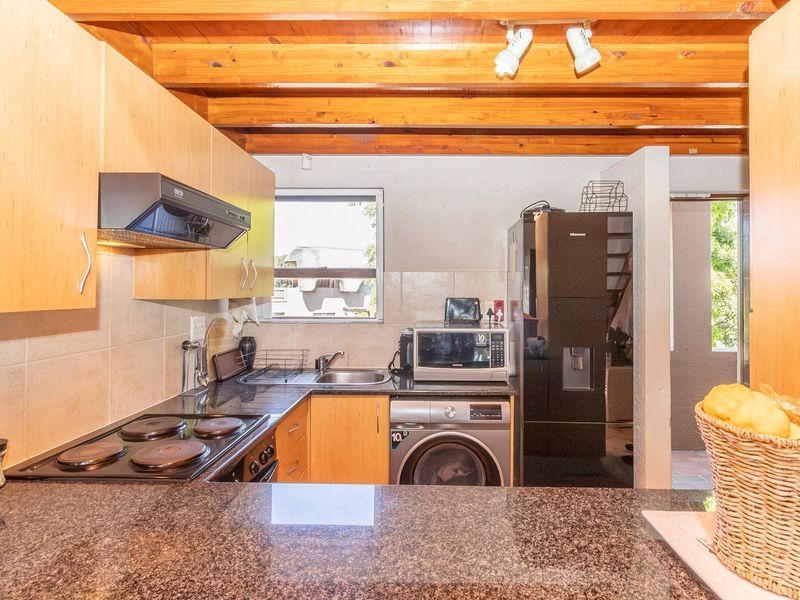 Functional kitchen featuring granite countertops, built-in cabinetry, electric hob, extractor fan, and exposed timber ceiling beams.